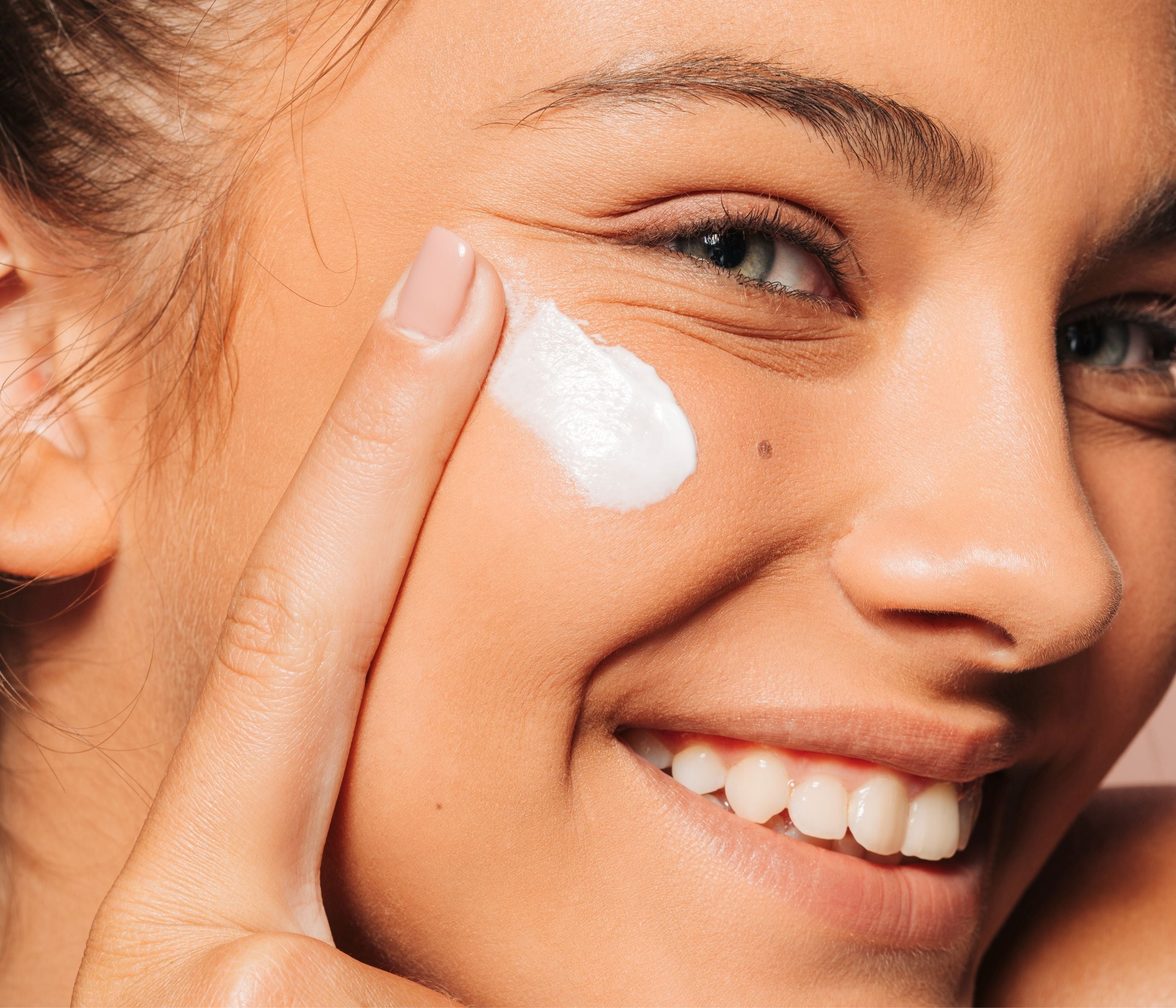 Junge lächelnde Frau trägt Creme auf ihre Wange auf.